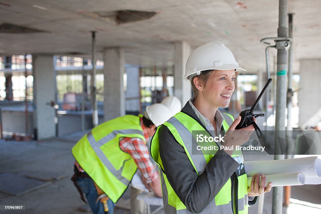 Mujer de negocios hablando en walkie talkie en solar de construcción - Foto de stock de Arquitecto libre de derechos