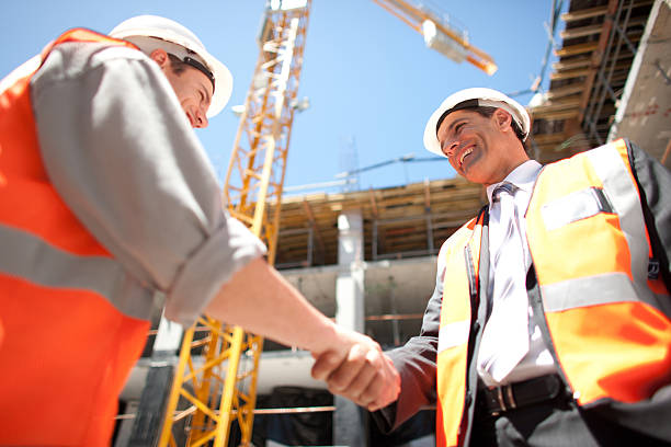 trabajadores de la construcción en sitio de construcción estrechándose las manos - hardhat construction men handshake fotografías e imágenes de stock