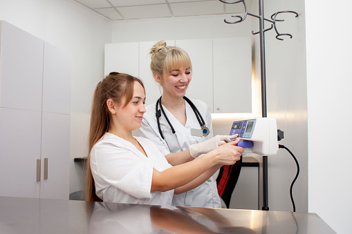 two female nurses in uniform connect an infusion pump in a hospital, young female doctors in medical gowns use medical equipment