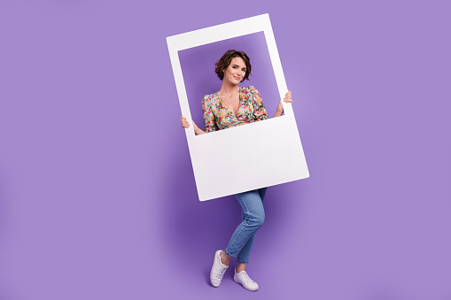 Full length photo of lovely young lady holding instant photo frame wear trendy flower print garment isolated on violet color background.