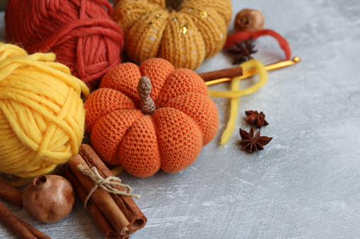 Autumn still life with woolen yarn balls, crocheted pumpkins, cinnamon sticks and anise on grey background with copy space. Cozy autumn concept.
