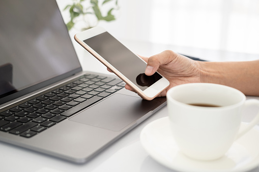 Asian businesswoman using laptop and checking smart phone, close up clean image in front of the window in soft light.