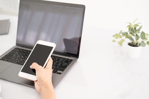 Asian businesswoman using laptop and checking smart phone, close up clean image in front of the window in soft light.