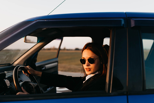 business woman in a jacket and sunglasses is driving a car. successful young woman driver