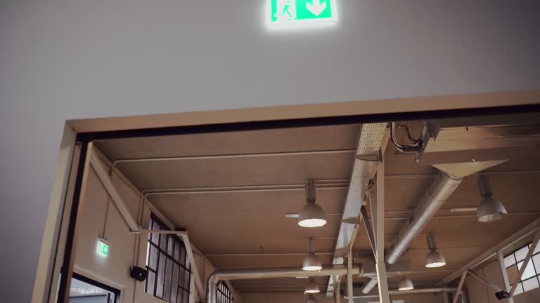 Green neon emergency exit sign hanging above the doorway entrance, illuminated down arrow and running person on the sign, directional guidance to escape in case of emergency