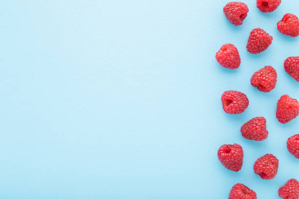 istock Fresh red raspberries on light blue table background. Pastel color. Closeup. Top down view. Empty place for text. 1709697347