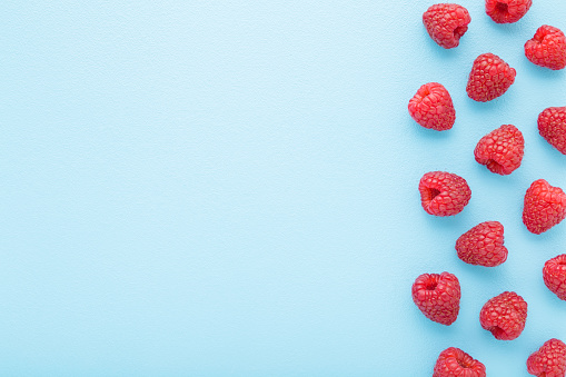 Fresh red raspberries on light blue table background. Pastel color. Closeup. Top down view. Empty place for text.