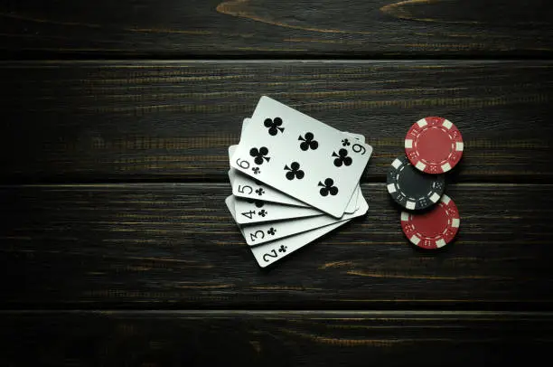 Photo of Popular poker game with straight flush winning combination. Cards with chips on a black vintage table in a poker club. Free black space for ads.