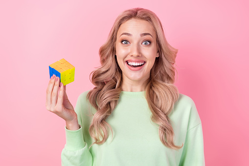 Closeup portrait of surprised crazy girl wear green pullover holding puzzle square toy eureka isolated on pastel pink color background.