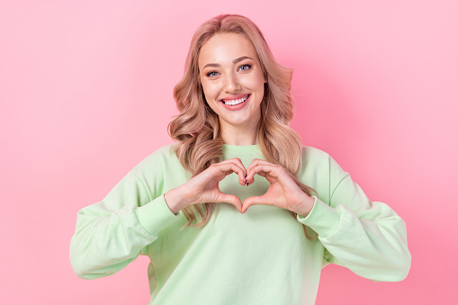 Portrait of lovely cheerful girl toothy smile arms fingers demonstrate heart symbol isolated on pink color background.