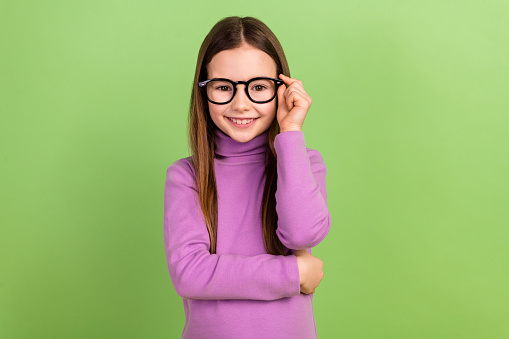 Photo of adorable smart kid with long hairstyle wear purple turtleneck touching eyewear at school isolated on green color background.