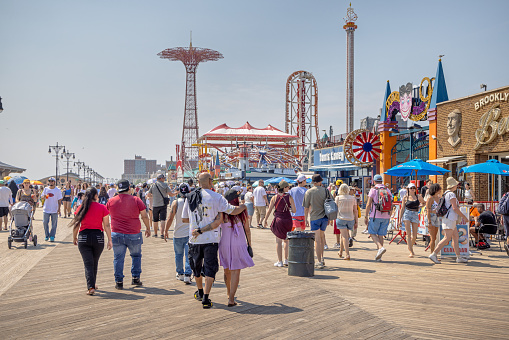 Coney Island, New York, USA - August 20th 2023:   People walking on the famous boardwalk outside the many amusement parks opposite the beach
