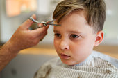 Barber cutting little boy's hair with scissors