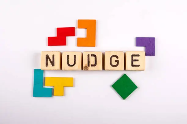 NUDGE. Wooden alphabet letters and colorful figures on a white background.