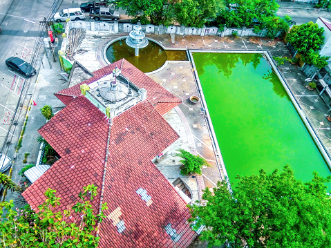 Bangkok, Thailand - 19 February 2018: House with red tile rooftop, fountain and swimming pool with dirty green standing water, top view. Abandon old motel and rectangle pool with stagnant water