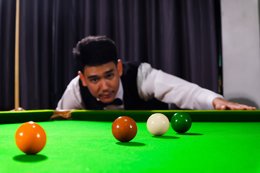 Snooker ball and snooker player with competitor blur while aiming black ball on snooker table in background.