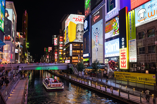 Osaka, Japan - November 24, 2016: Tourist people on sailing boat to visit Dotonbori district at night, Kansai. Famous travel landmark to view Glico advertisement banner.