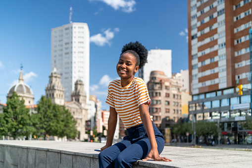 Cute young african woman sitting on an urban park with city views