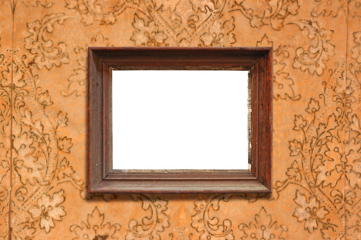 An old picture frame hangs on a wall with old wallpaper from the early 20th century.