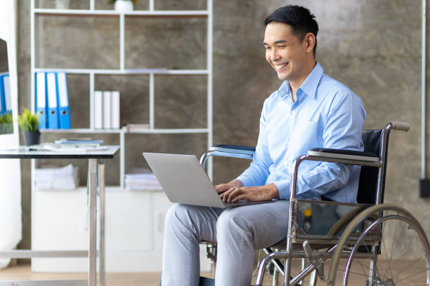 istock Man in wheelchair using laptop in office. 1709868162