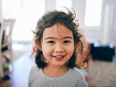 A happy multiracial three year old girl in a home.