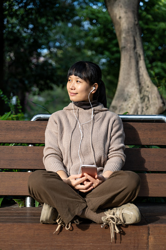A woman is sitting on a park bench resting with her phone