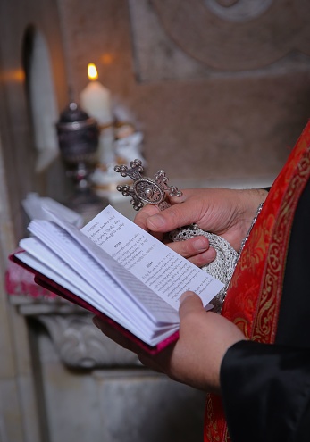 Closeup of the hands of a religious leader clutching a bible and a cross, symbolizing faith and devotion