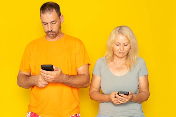 istock Middle aged couple looking at their cell phone ignoring each other isolated on yellow studio background. Concept of social distancing due to technology. 1709875169