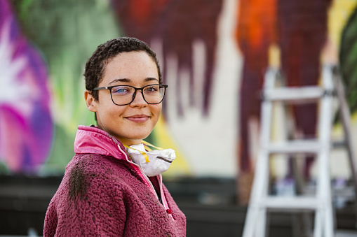 Portrait of Young Mexican woman creating outdoor mural on the roof top wall. She is dressed in casual outfit. Exterior of old building in the city of Toronto, Canada..