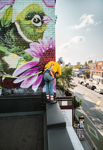 Young Caucasian woman creating outdoor mural on the roof top wall. She is dressed in casual outfit. Exterior of old building in the city of Toronto, Canada..
