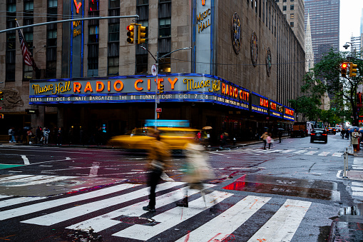 New York City, USA - September 30, 2023: Radio City Music Hall at dusk in a rainy day. Street view of traffic and people walking on the street, Slow motion, New York City