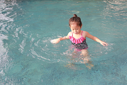 Adorable little Asian child girl has fun playing in the pool.
