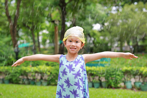 Happy little Asian girl wearing plastic bag (Emergency cap) on head having fun in the summer rain.
