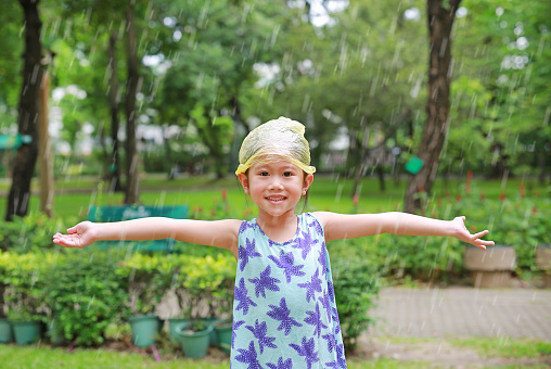 Adorable little Asian child girl wearing plastic cap on head is happy with the rain.