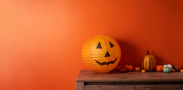 Halloween decorations on wooden table against orange background. Wide banner with place for text.