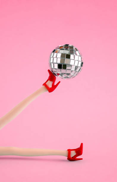 istock Doll legs in red shoes with disco ball on pink background. 1709918270