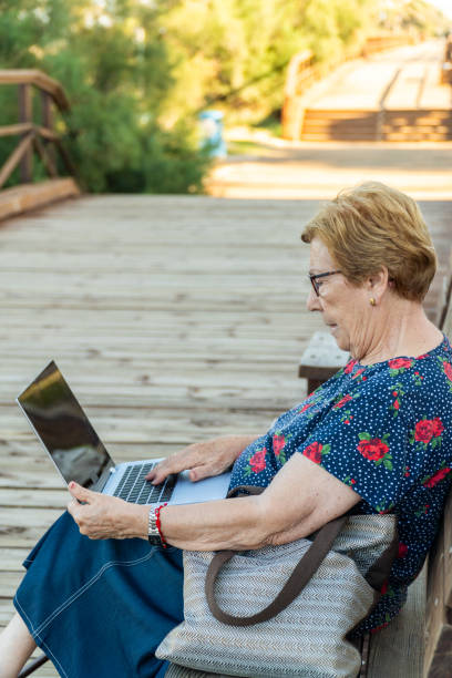 istock Elderly woman sitting on a bench using a laptop. Side view. 1709935098
