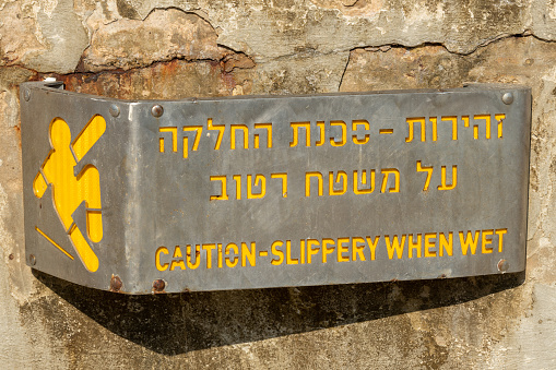 Tel Aviv, Israel September 9, 2022 Caution slippery when wet metal sign with yellow lettering in Hebrew and English in Israel.