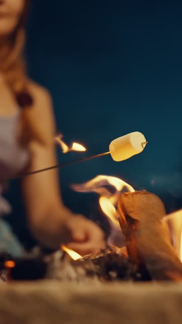 Close-up of Blurred Woman Roasting Marshmallow on Skewer over Bonfire at Night - VERTICAL