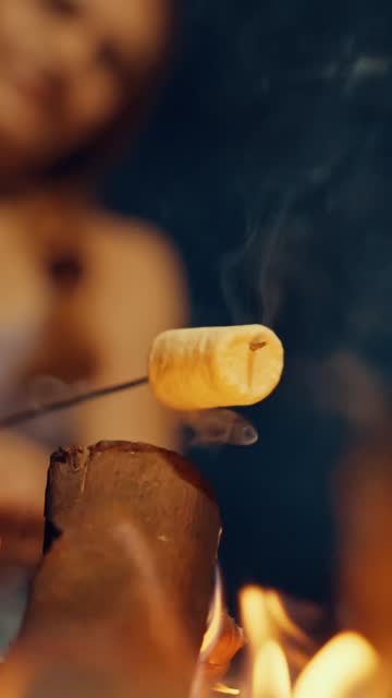 Close-up of Blurred Woman Roasting Marshmallow on Skewer over Bonfire at Night - VERTICAL