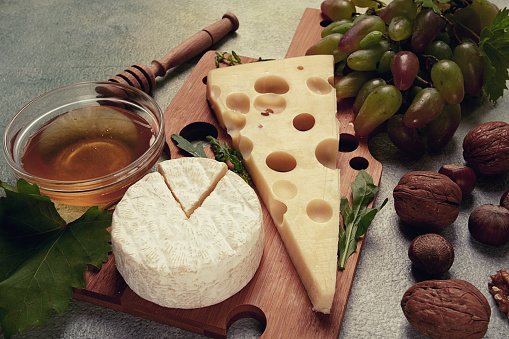 cheese with big holes, emmental, maasdam, brie cheese, on a cutting board, with grapes and honey, nuts, appetizer to wine, top view,