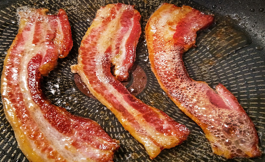 Gourmet juicy, crunchy, sizzling belly bacon strips, fried in non stick frying pan - detail, high resolution stock photography.