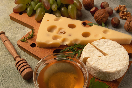 cheese with big holes, emmental, maasdam, brie cheese, on a cutting board, with grapes and honey, nuts, appetizer to wine, top view,