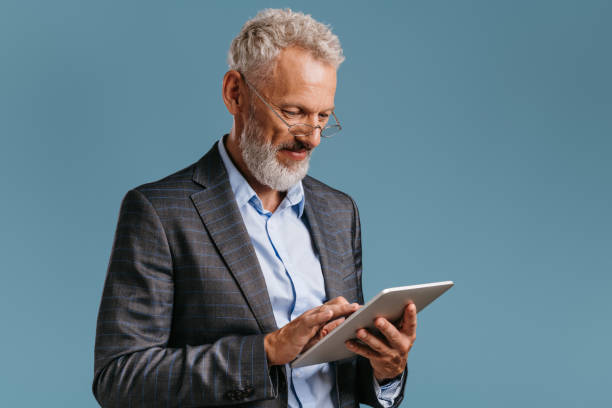 istock Confident mature businessman working on digital tablet while standing on colored background 1709979269
