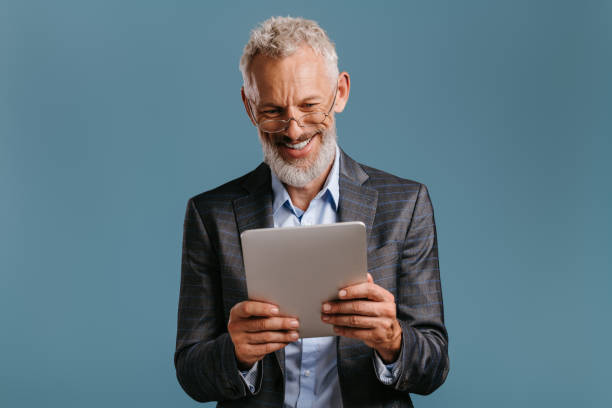 istock Confident mature businessman holding digital tablet and smiling while standing on colored background 1709979821