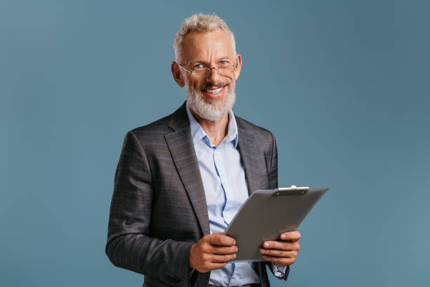 istock Confident mature businessman holding file folder and smiling while standing on colored background 1709979826