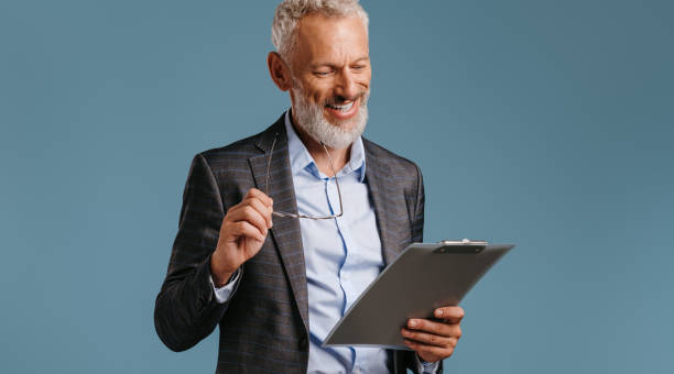 istock Confident mature businessman looking at clipboard smiling while standing on colored background 1709982093