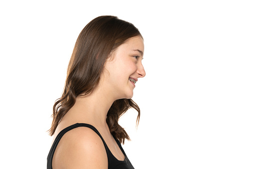 Profile of a beautiful young smiling women with long hair, no makeup and dental braces on a white studio background.