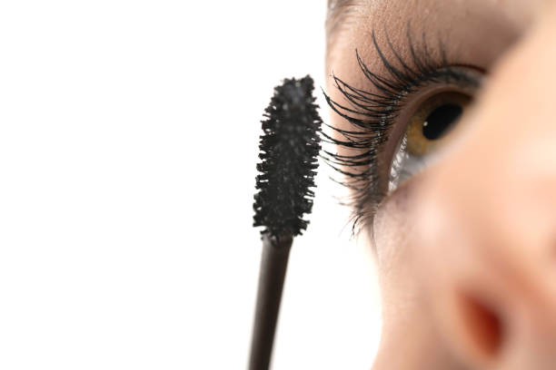 Macro closeupt of a young woman applying mascara with brush on a white background Macro closeupt of a young woman applying mascara with brush on a white studio background teenage girl before and after make up stock pictures, royalty-free photos & images