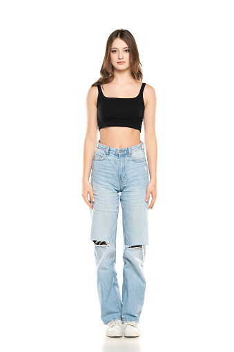Young female model wearing ripped jeans and black sleeveless shirt posing on a white studio background. Front view